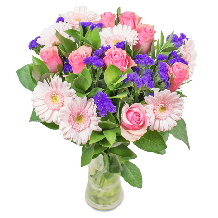 A striking floral arrangement presented in a clear glass vase, styled against a clean, white backdrop and echoing the timeless grace of Harrow on the Hill. At its core, 7 to 9 pink roses in shades from soft blush to deep rose are artfully staged, their petals either tightly wrapped or just unfurling into elegant spirals, reminiscent of the historic charm found along Grove Hill. Complementing them are 5 to 7 pale pink gerbera daisies, their broad, dainty faces and paler centers evoking the welcoming vibe of a local café terrace. Accents of vivid purple statice wind through the display, lending captivating texture and bursts of colour - a nod to the creative vibrancy found within the village. The entire bouquet is enveloped in abundant green foliage, lending an air of natural abundance, like the foliage traced along the borders of Harrow School's fields. Stems are visible through the fresh, clear water of the vase, completing this vision of modern freshness and delicate balance. This arrangement, available for delivery across Harrow on the Hill, is an ideal choice for birthdays, anniversaries, or simply infusing home or office with joy, affection, and the distinctive beauty of our neighbourhood.