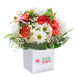 A celebration of colour and joy, this bouquet radiates warmth from its place inside a spotless square white gift bag, beautifully echoing the charm of Harrow on the Hill's leafy streets. Coral and peach carnations burst open in ruffled waves, weaving amidst clusters of bright white daisies that sparkle with golden-green centers, each one evoking a burst of laughter or a kind word shared. Wisps of baby's breath mingle delicately, their cloud-like blossoms adding a dreamy softness that carries a sense of gentle innocence-a nod to the tranquil corners of Harrow's local gardens. Tucked subtly to one side, unopened buds with a faint purple blush hint at new beginnings and hidden delights. All these vibrant flowers are embraced by a lush collar of polished deep green foliage, the leaves glistening softly under the careful illumination of studio lighting. The bouquet's rounded, abundant form conveys both opulence and approachability, while the white bag's ribbon handles suggest thoughtful preparation for easy gifting-whether to mark an anniversary, a birthday, or simply to spread happiness nearby. This arrangement, crafted with skill and care, offers a beautiful reminder of the simple pleasures of giving, delivered across Harrow on the Hill with the expertise of local florists.